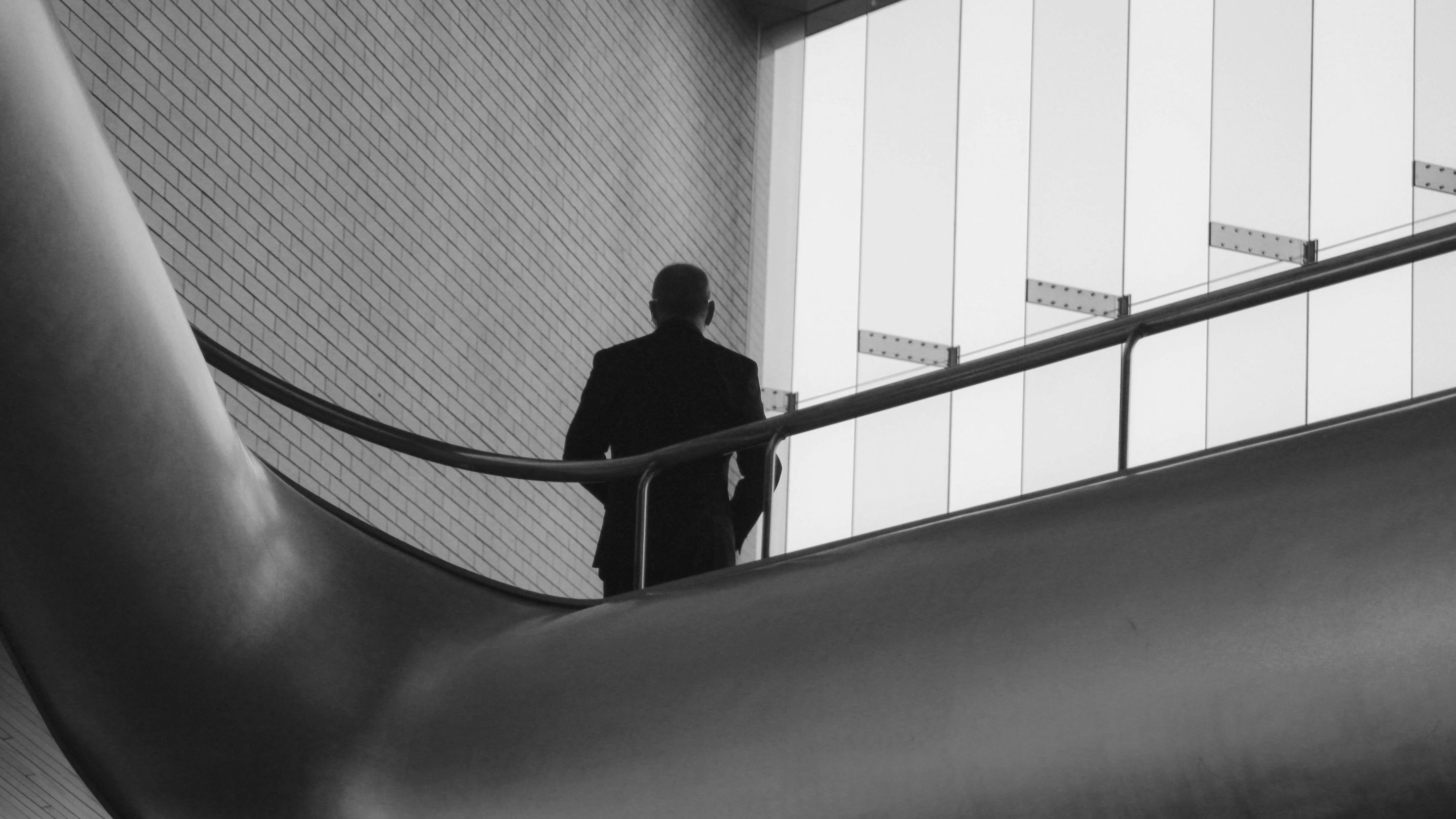 Black and white photo of a man in a suit leaning against a staircase railing looking at his phone